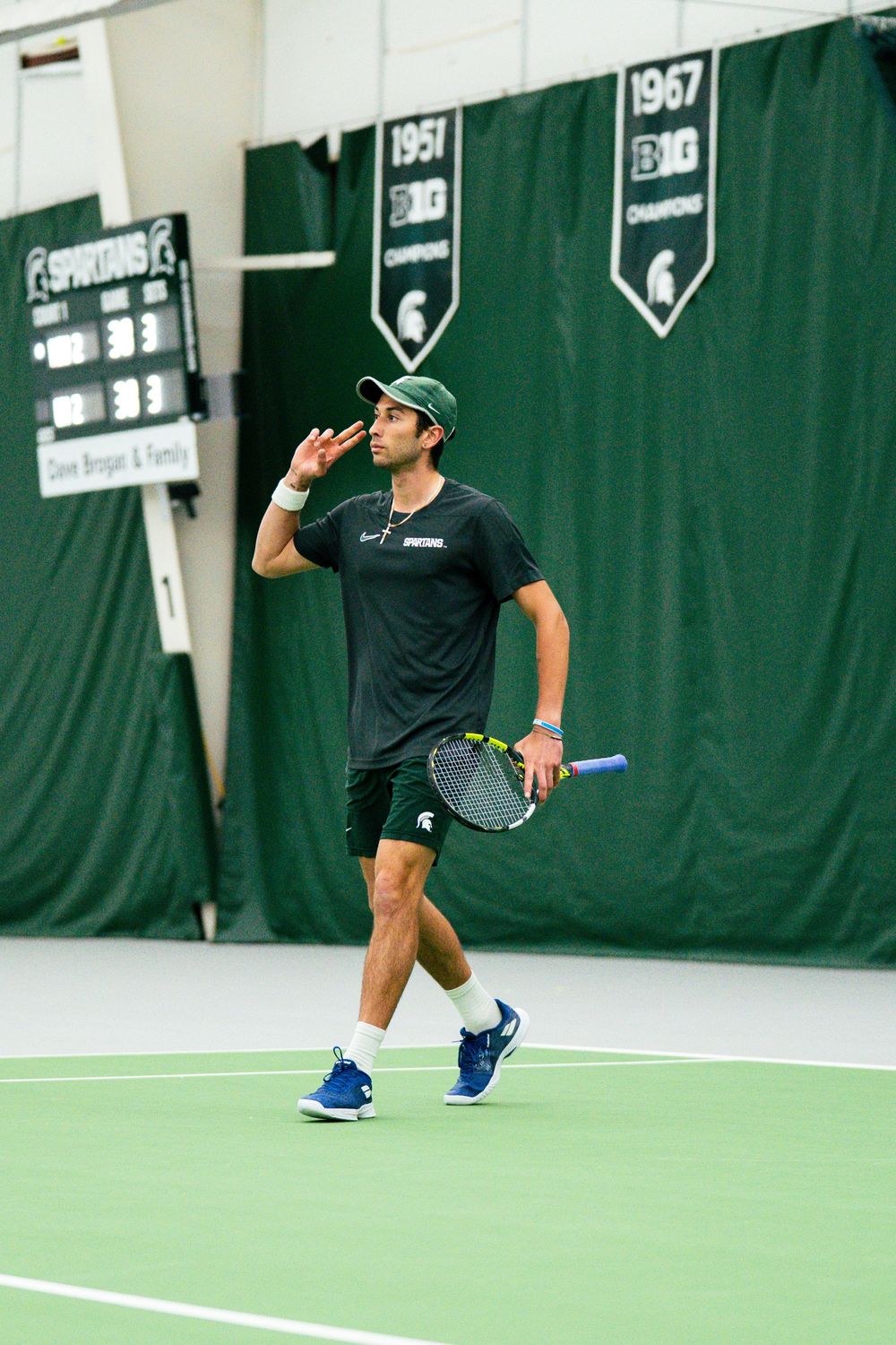 Ozan Baris on court at the MSU Tennis Center beneath the 1967 Big Ten Champions banner